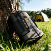 Minener NightScout Ridge night vision binoculars resting beside a tree at a campsite, showcasing the rugged black body for camping and outdoor exploration.